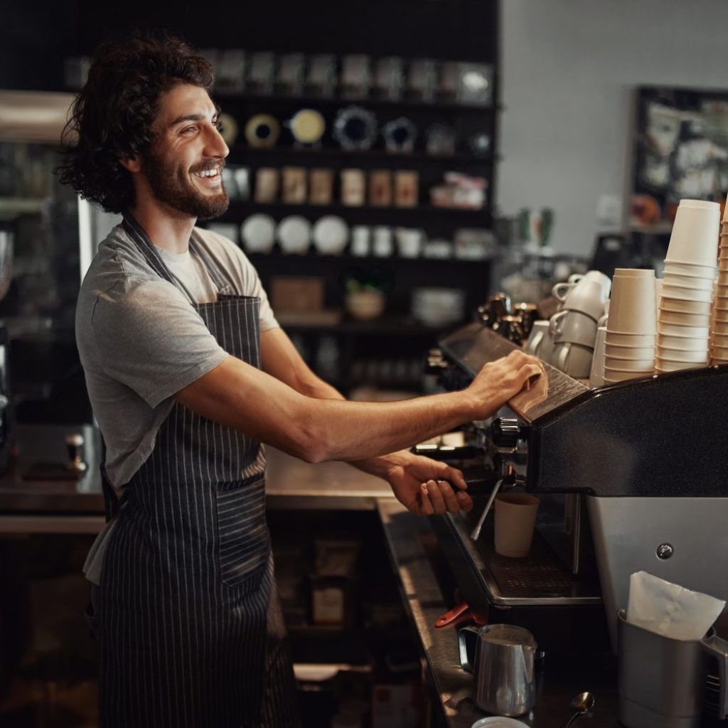 Smiling handsome waiter making coffee in cafeteria using coffee machine